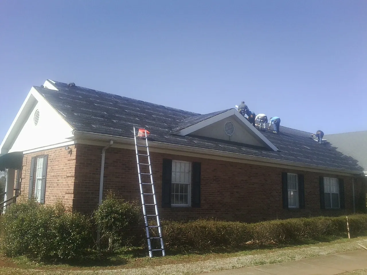 Crew tearing shingles off a brick ranch roof with a ladder set — Emergency Roof Repair work by our crew in Plymouth