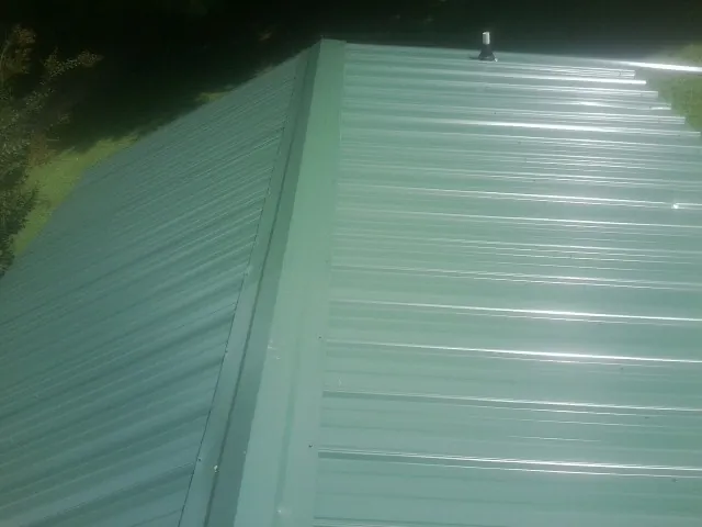 New green metal panels meeting at the ridge of a roof — Flat Roof Repair work by our crew in Plymouth